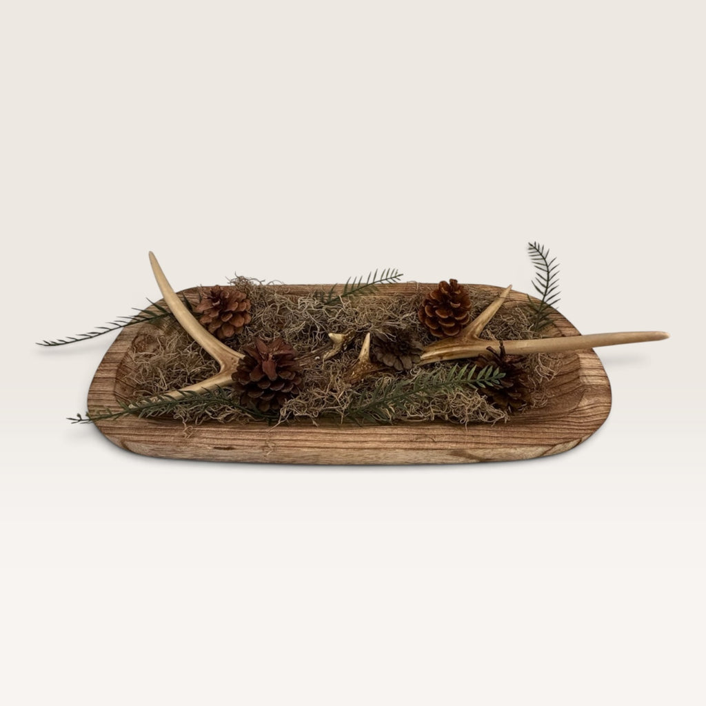 Side view of rustic antler dough bowl centerpiece with evergreen greenery, moss, and pinecones