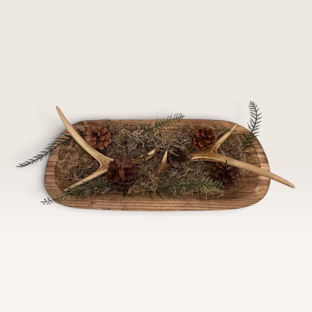 Rustic wood dough bowl arrangement featuring pinecones, greenery, moss, and faux antler accents