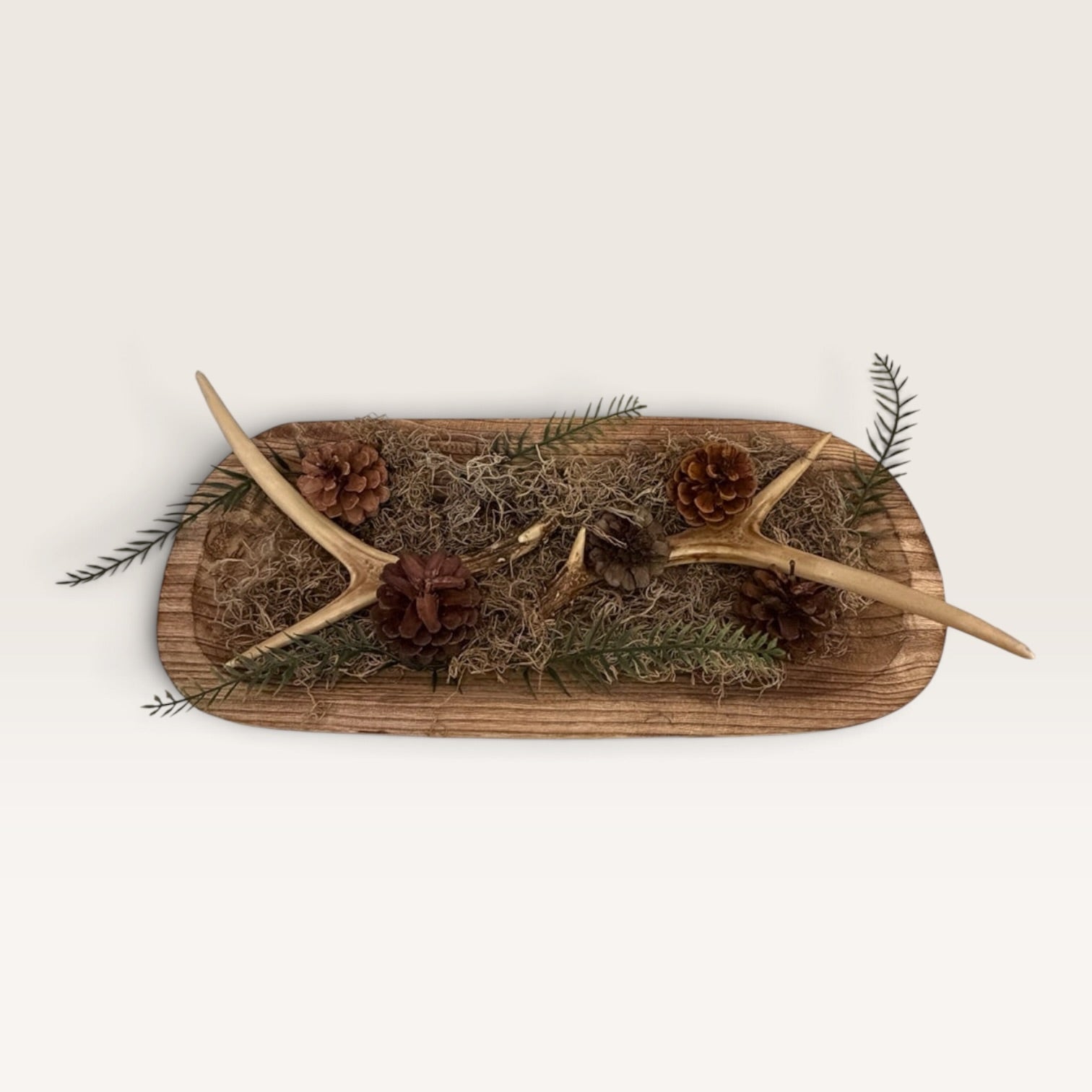 Rustic wood dough bowl arrangement featuring pinecones, greenery, moss, and faux antler accents