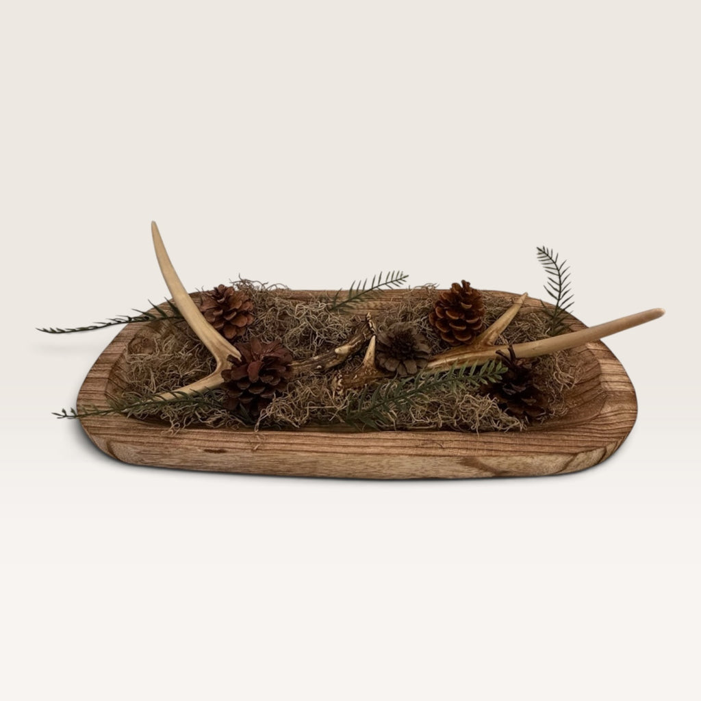 Rustic wood dough bowl centerpiece with evergreen greenery, pinecones, moss, and realistic faux antler accents