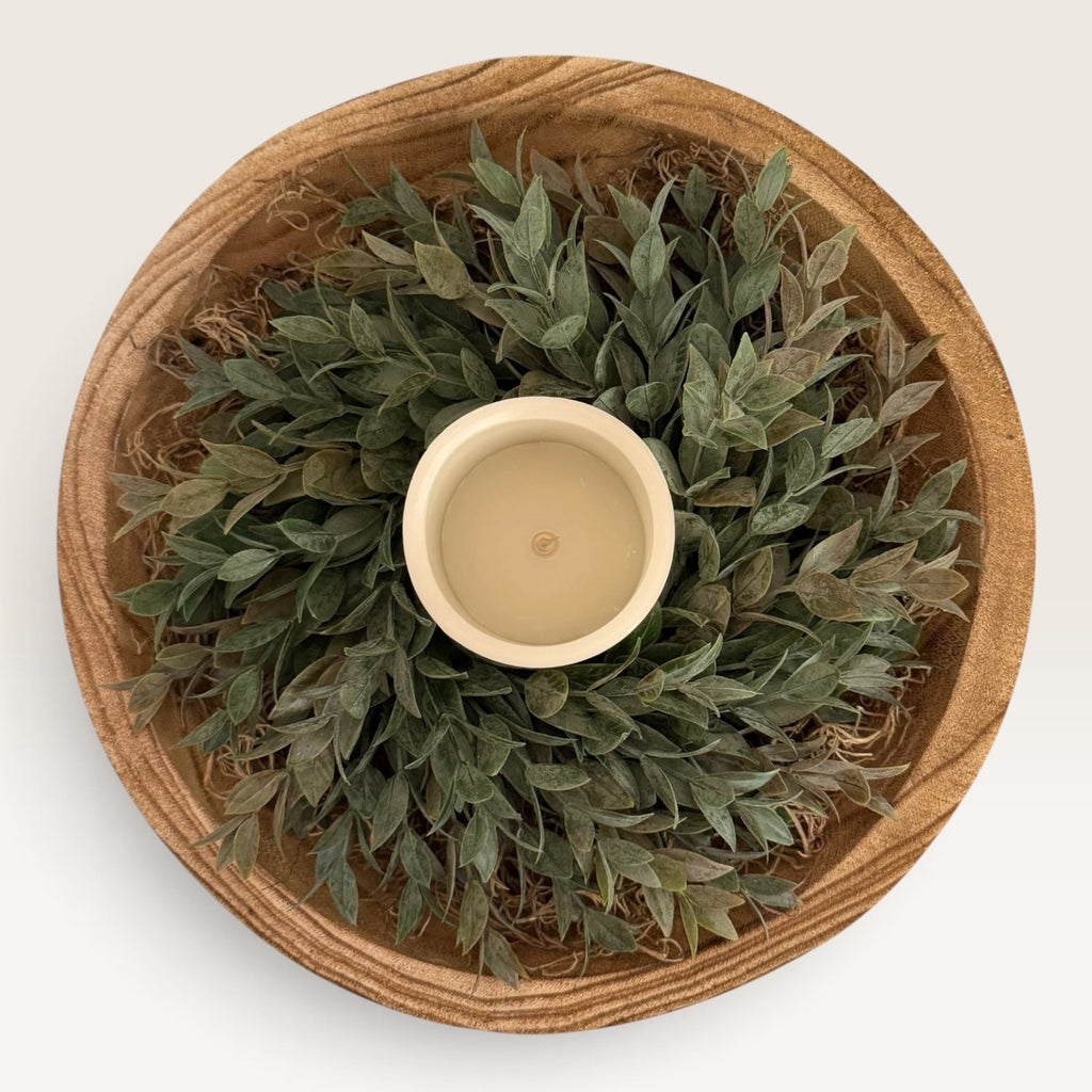 Overhead view of wood bowl centerpiece with faux greenery and LED pillar candle