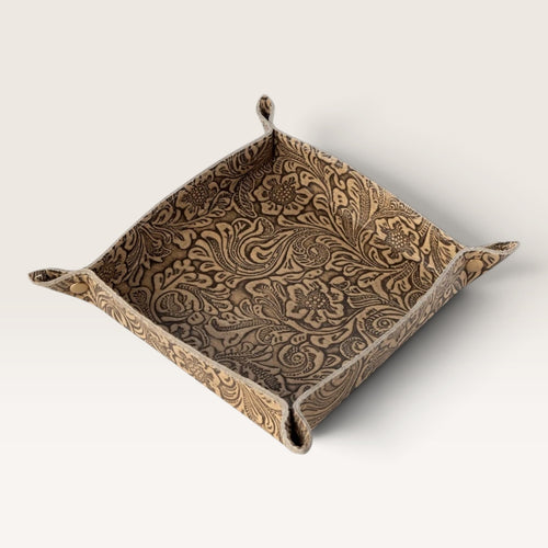 A square fabric tray with a raised rim and small hanging tabs at the corners, featuring an embossed floral and scroll pattern in warm brown and beige tones, shown on a light gray background.