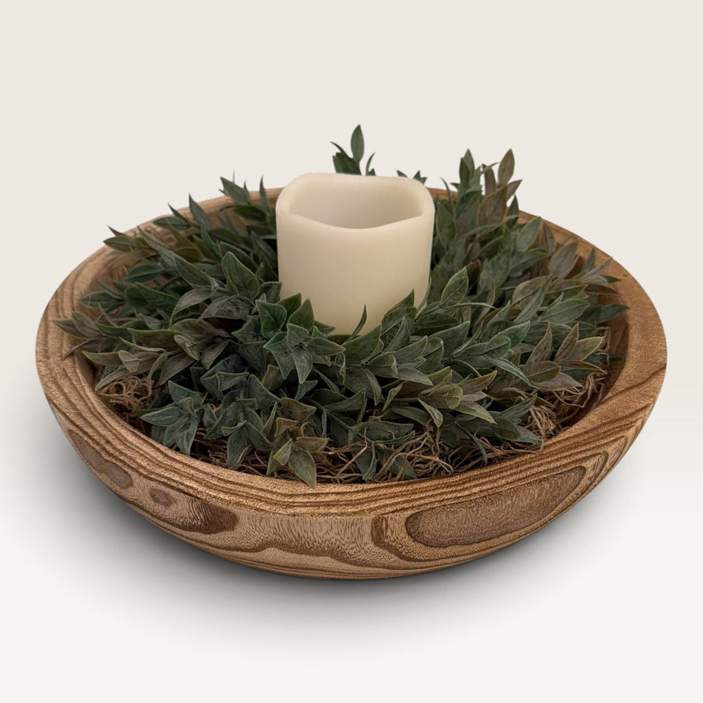 Angled view of rustic wood bowl centerpiece with greenery and flameless candle