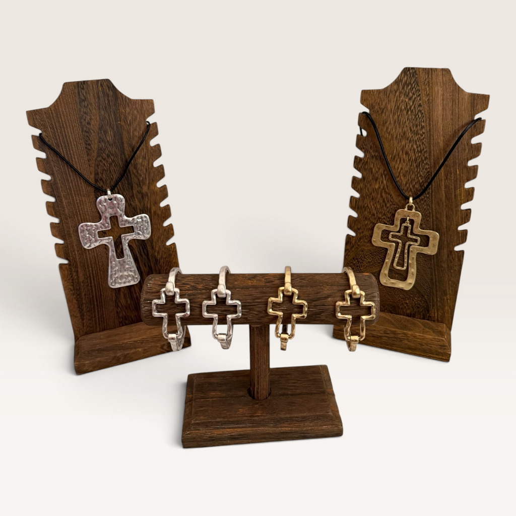 Red Clay Mercantile hammered silver and gold cross pendant necklaces and matching bracelets on wooden displays.