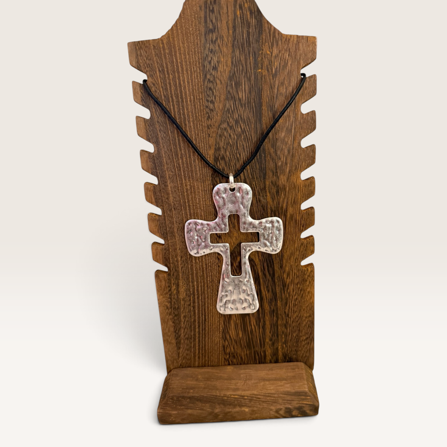 Red Clay Mercantile silver hammered cross pendant on a black cord displayed on a rustic wooden jewelry stand